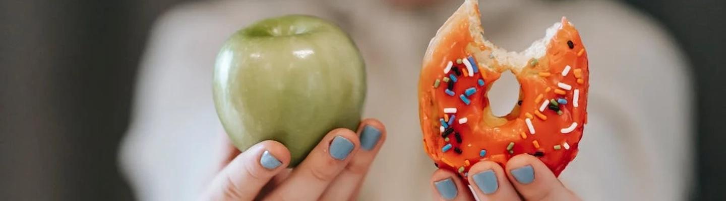 Frau hält Apfel und angebissenen Donut hoch: Wie lässt sich bei Diabetes abnehmen?