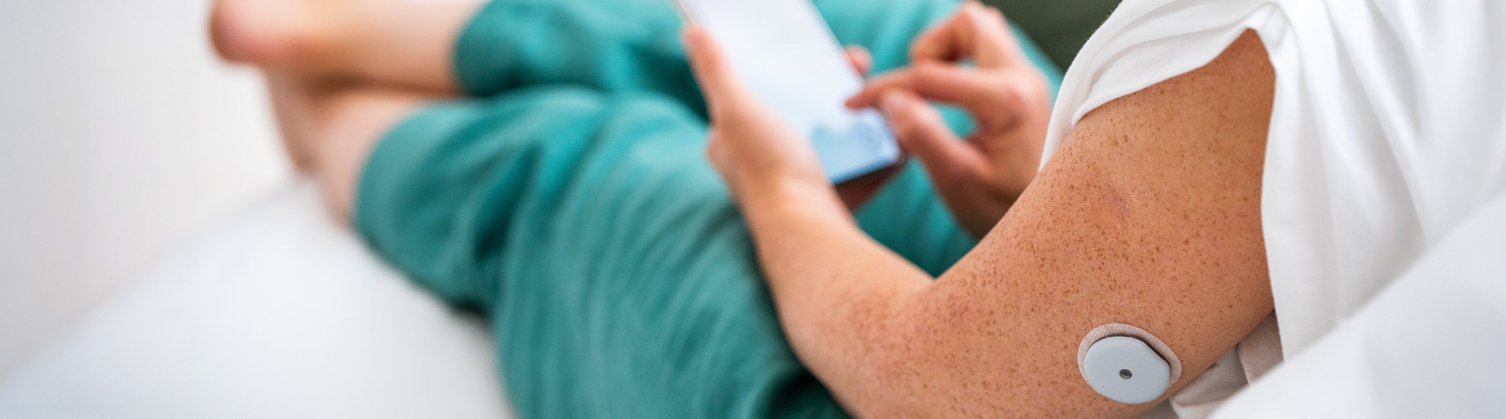 Person hält ein Smartphone mit der Accu-Chek SmartGuide App neben ihrem Arm, an dem ein CGM-Sensor sitzt