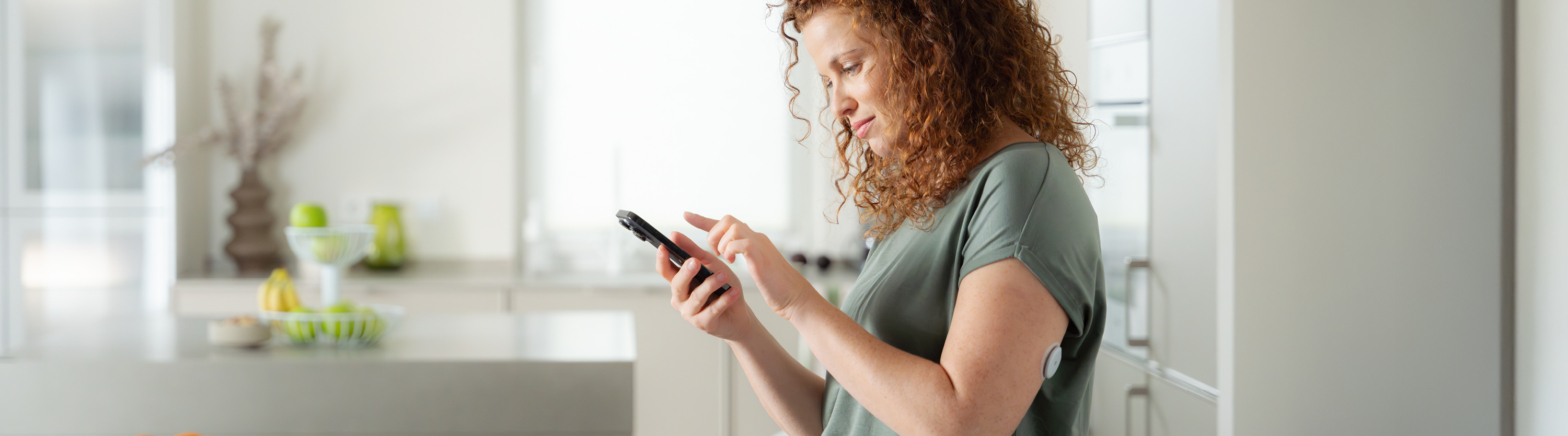 Frau steht in der Küche und schaut auf ihr Smartphone mit der Accu-Chek SmartGuide App