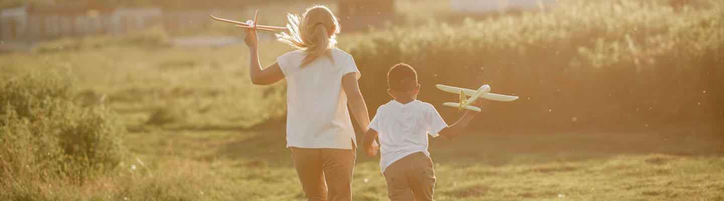 Diabetes bei Kindern: 2 Kinder rennen mit Flugzeugen über eine Wiese.