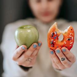 Frau hält Apfel und angebissenen Donut hoch: Wie lässt sich bei Diabetes abnehmen?