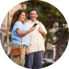 Zwei Personen stehen nebeneinander und schauen gemeinsam lächelnd auf ein Smartphone mit der Accu-Chek SmartGuide App